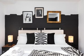 Un dormitorio con una cama, dos mesitas de noche, un espejo y tres cuadros en la pared.