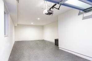 Een kamer met een grijze vloer, witte muren, een aan het plafond gemonteerde projector en een kleine, zwarte prullenbak.