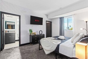 Un dormitori modern amb un llit, una petjadura, una televisió que mostra 'NETFLIX' i una finestra amb vistes.