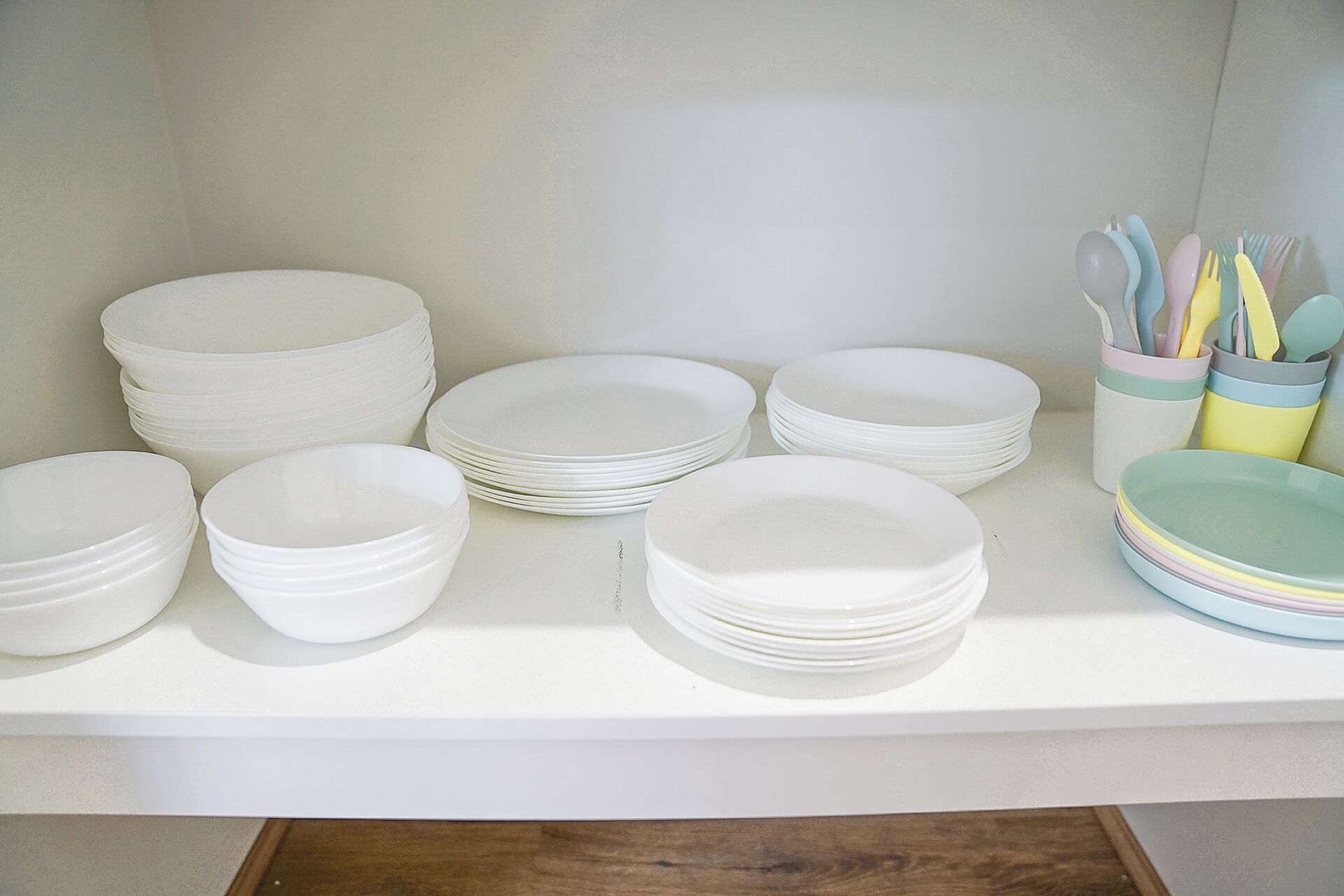 A kitchen counter with stacks of white plates and bowls, and a utensil holder with spoons and forks.