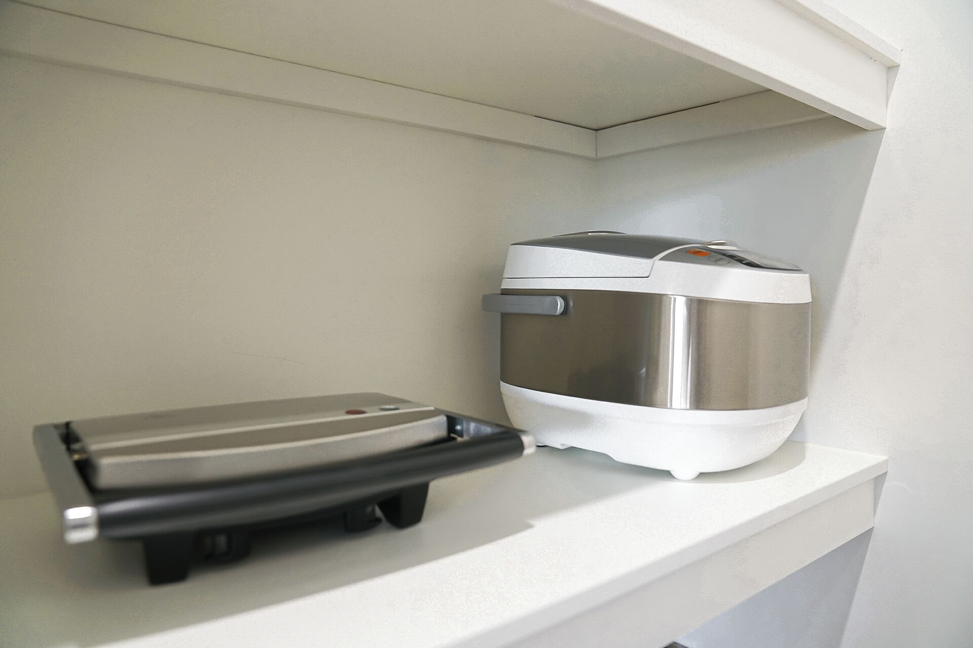 A compact kitchenette with a stainless steel coffee maker and a black electric kettle on a white countertop.