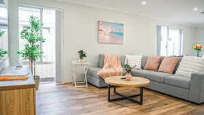 Una sala de estar moderna con un sofá gris, una mesa de centro redonda de madera y una pequeña mesita auxiliar blanca con una planta.