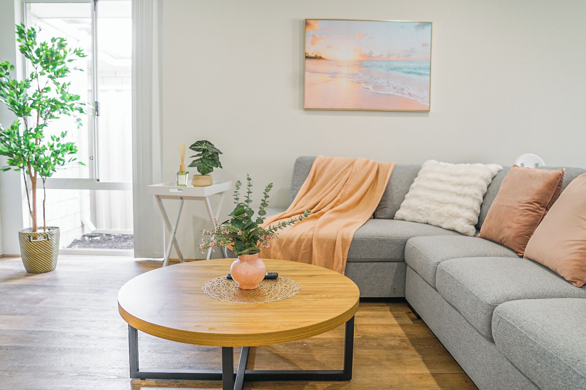 A living room with a grey sofa, a round wooden coffee table, and a painting of a beach scene on the wall.