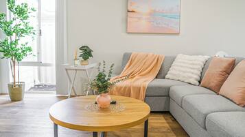 A living room with a grey sofa, a round wooden coffee table, and a painting of a beach scene on the wall.