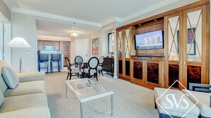 Ein großzügiges Wohnzimmer mit Fernseher, Essbereich und einer Küche im Hintergrund.