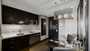 Une cuisine moderne avec des meubles de couleur sombre, un four à micro-ondes en acier inoxydable, un évier et un coin repas comprenant une table et des chaises en verre.