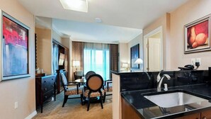 A hotel room with a dining area, a kitchen with a sink, and a large window with curtains. - SVS: 2BD Mountain View Suite | Private Balcony | Full Kitchen | MGM (Las Vegas)