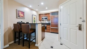 A compact kitchen with a central island, wooden cabinets, and a microwave. - SVS: 2BD Mountain View Suite | Private Balcony | Full Kitchen | MGM (Las Vegas)
