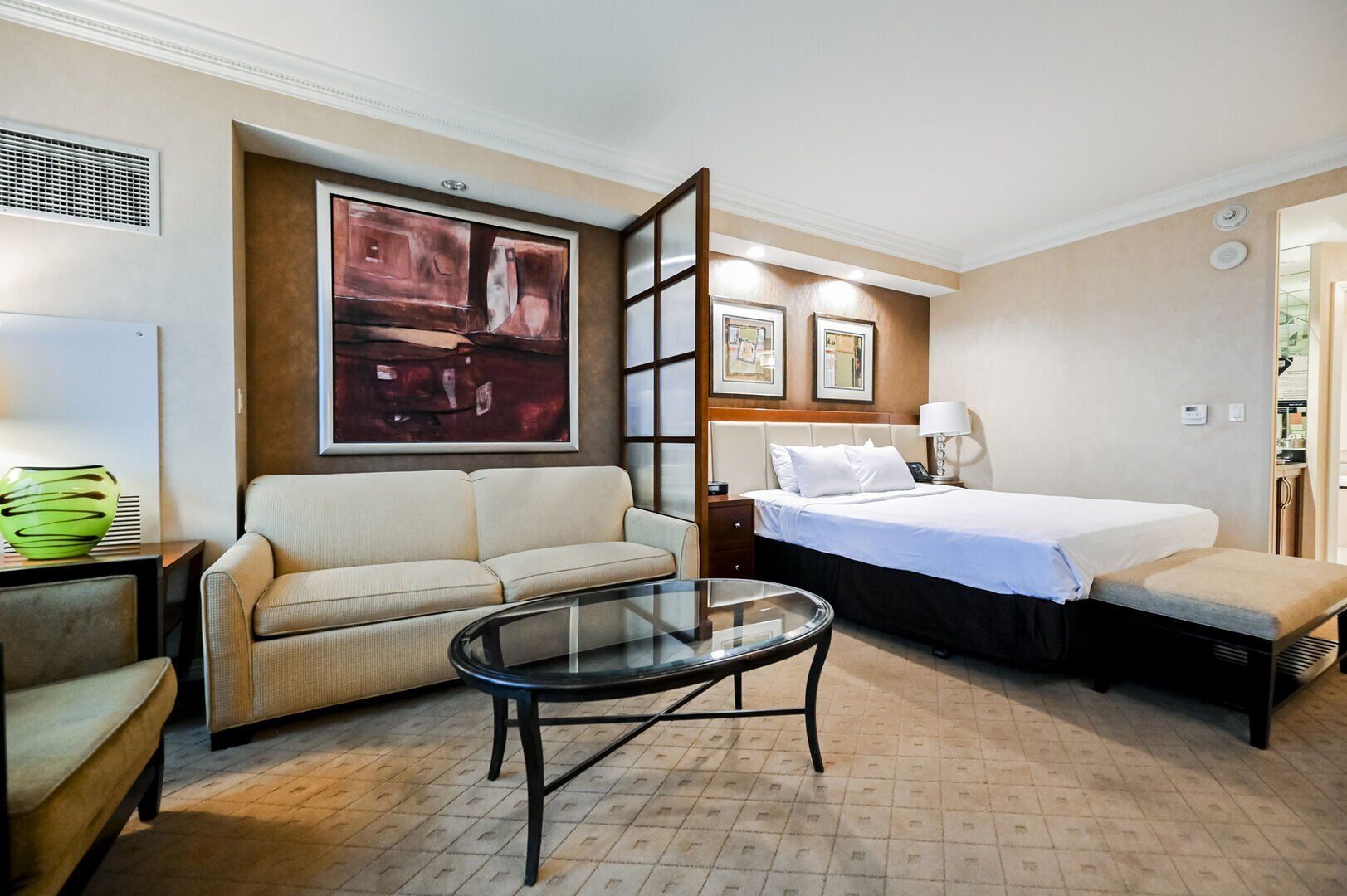 Una habitación de hotel con una cama, un sofá, una mesa de vidrio y un cuadro en la pared.