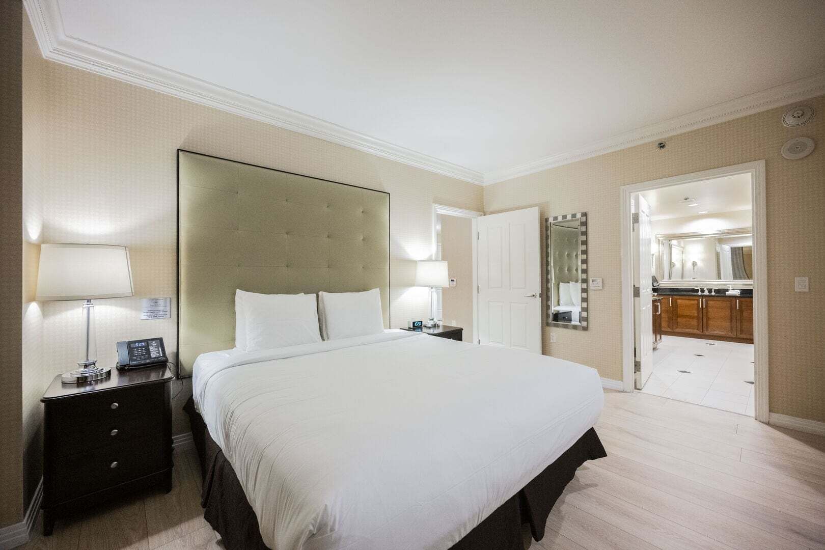 Une chambre d’hôtel avec un grand lit, des lampes de chevet, une table de nuit, un miroir et une vue sur la salle de bain.