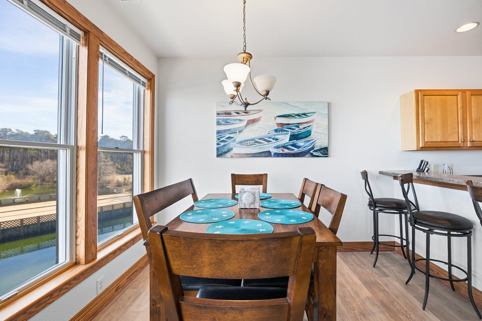 A dining area with a wooden table, chairs, and a view of boats through large windows.