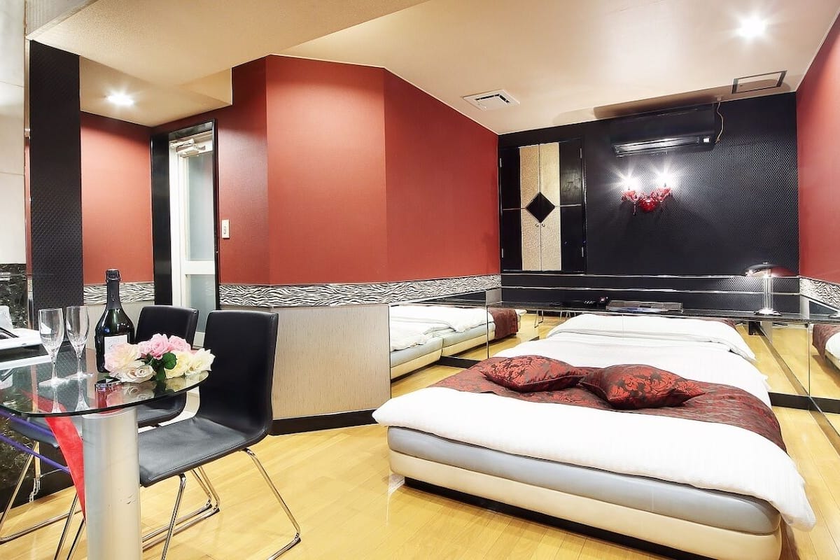 A modern hotel room with a bed, a glass table with chairs, and a small seating area.