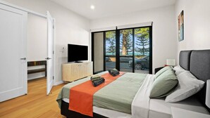 Een moderne slaapkamer met een bed, een televisie op een houten kast en uitzicht op het groen door grote ramen.