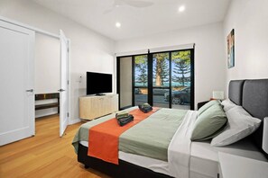 Ein modernes Schlafzimmer mit Bett, Fernseher auf einer Holzkommode und Blick ins Freie durch große Fenster.