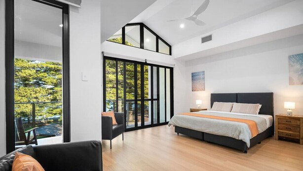 Een moderne slaapkamer met een groot bed, een sofa en een balkon met uitzicht op bomen.