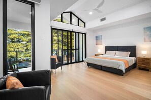 Un dormitorio moderno con una cama grande, un sofá y un balcón con vistas a árboles.
