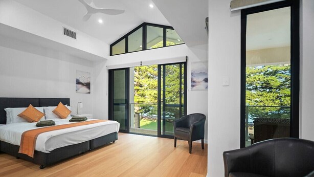 Ein modernes Schlafzimmer mit einem großen Bett, einem Sessel und einem Balkon mit Blick auf Grünflächen.