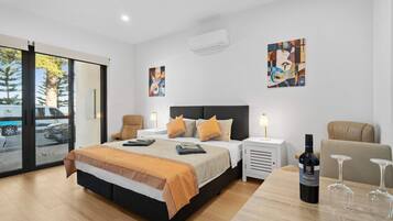 A modern hotel room with a large bed, two bedside tables, a desk with a chair, and a dining table with wine glasses.