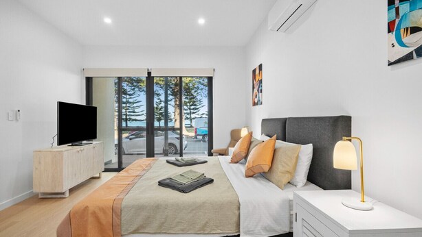Quarto moderno com cama, mesa de cabeceira, televisão e vista para o exterior.