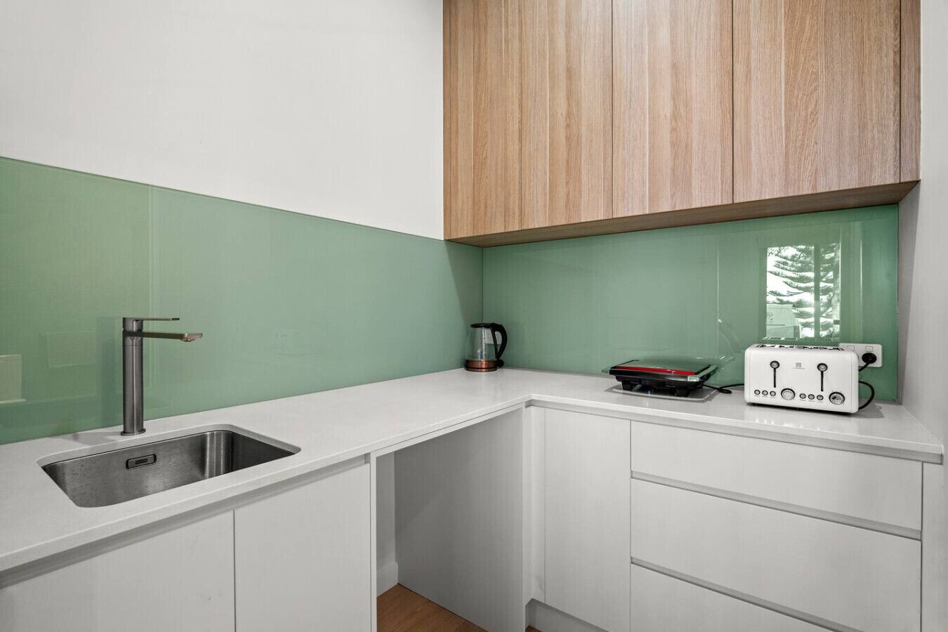 A compact kitchen with a sink, a kettle, and a toaster on the countertop.