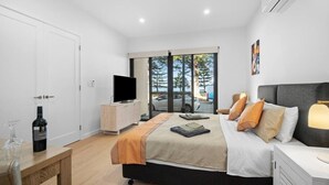 Quarto moderno com uma cama grande, uma TV em um armário de madeira, uma garrafa de vinho e vista para o exterior por grandes janelas.