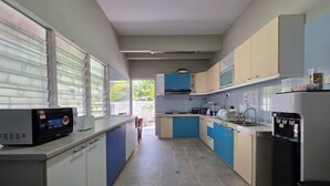 A kitchen with blue and white cabinets, a microwave, a water dispenser, and a window with blinds. - Room at Macalister near to LohGuanLye (George Town)