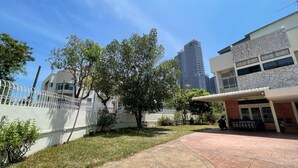 A courtyard with a paved walkway, a tree, and a building with a white facade and a stone-patterned wall. - Room at Macalister near to LohGuanLye (George Town)