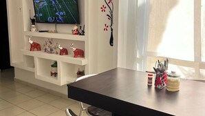 A modern living room with a flat-screen TV mounted on a white wall, a dining table with chairs, and a window providing natural light. - Diamond zone apartment with pool (Acapulco de Juárez)