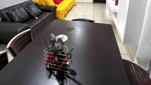 A dining area with a dark wooden table, a metal utensil holder, a black leather couch, and a yellow sofa with red cushions. - Diamond zone apartment with pool (Acapulco de Juárez)