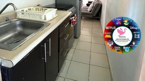 A compact kitchen with a sink, stove, and refrigerator. A dining area is visible in the background. - Diamond zone apartment with pool (Acapulco de Juárez)