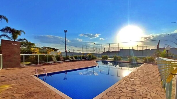 Una piscina rectangular con pavimento de piedra, rodeada por una valla y bañada por el sol.