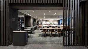 Un restaurant modern amb una barra llarga, diverses taules i una cuina visible a l'esfondri.