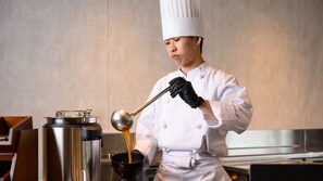Un chef con uniforme y gorro blancos sirve líquido de una olla a un bol.