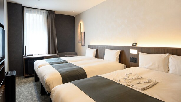 Ein Hotelzimmer mit zwei Betten, einem Schreibtisch, einem Stuhl, einem Fernseher und einem Fenster mit Vorhängen.