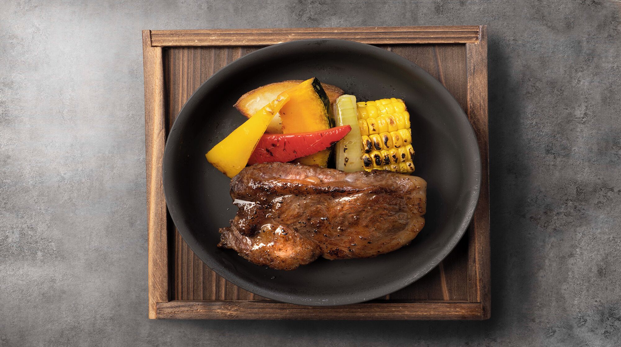 Ein Teller mit gegrilltem Steak, Maiskolben und gegrilltem Gemüse.