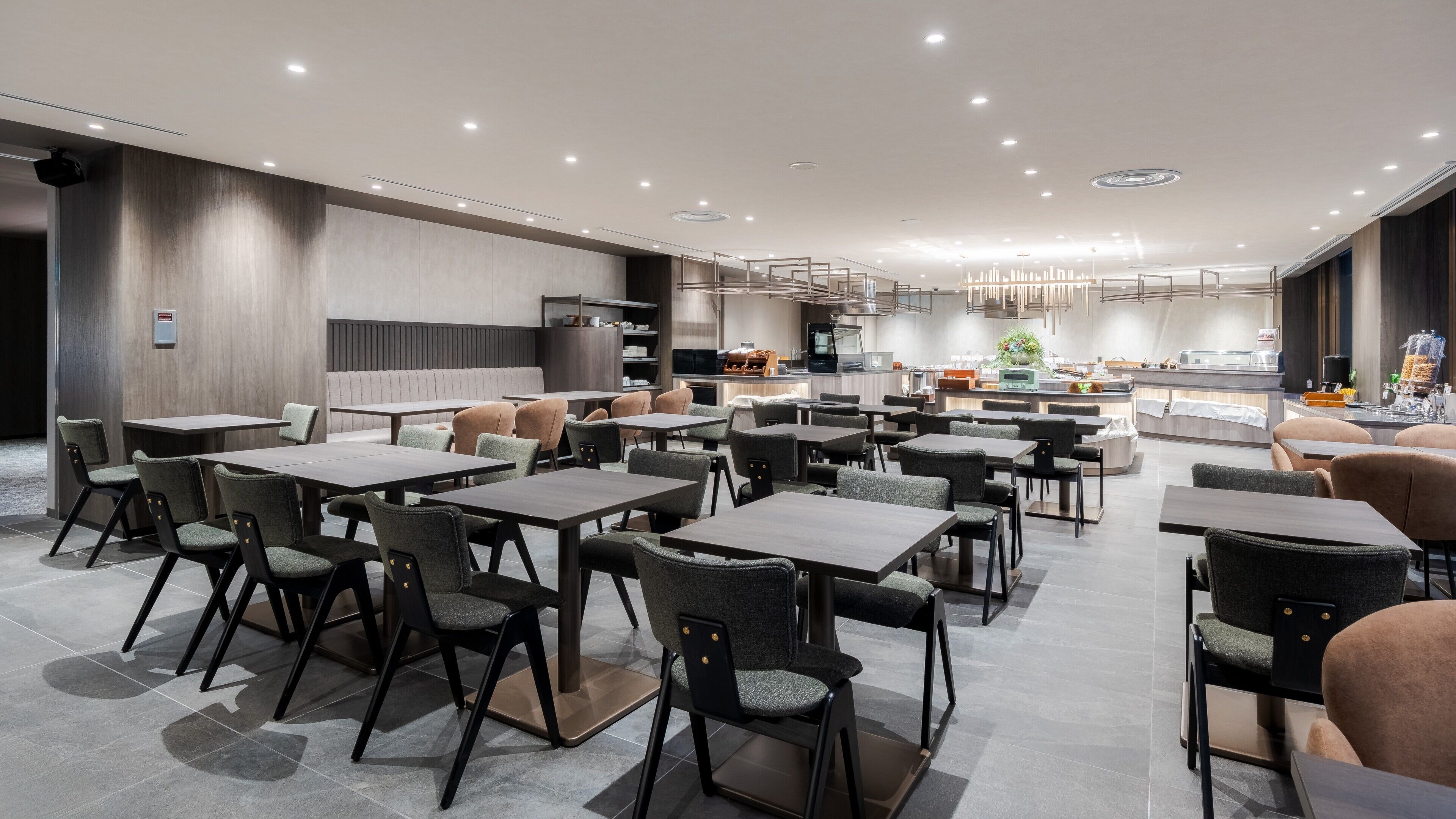 Ein modernes Restaurant mit mehreren Esstischen und Stühlen, einer Küchenzeile und einer Sitzecke mit Sofas.