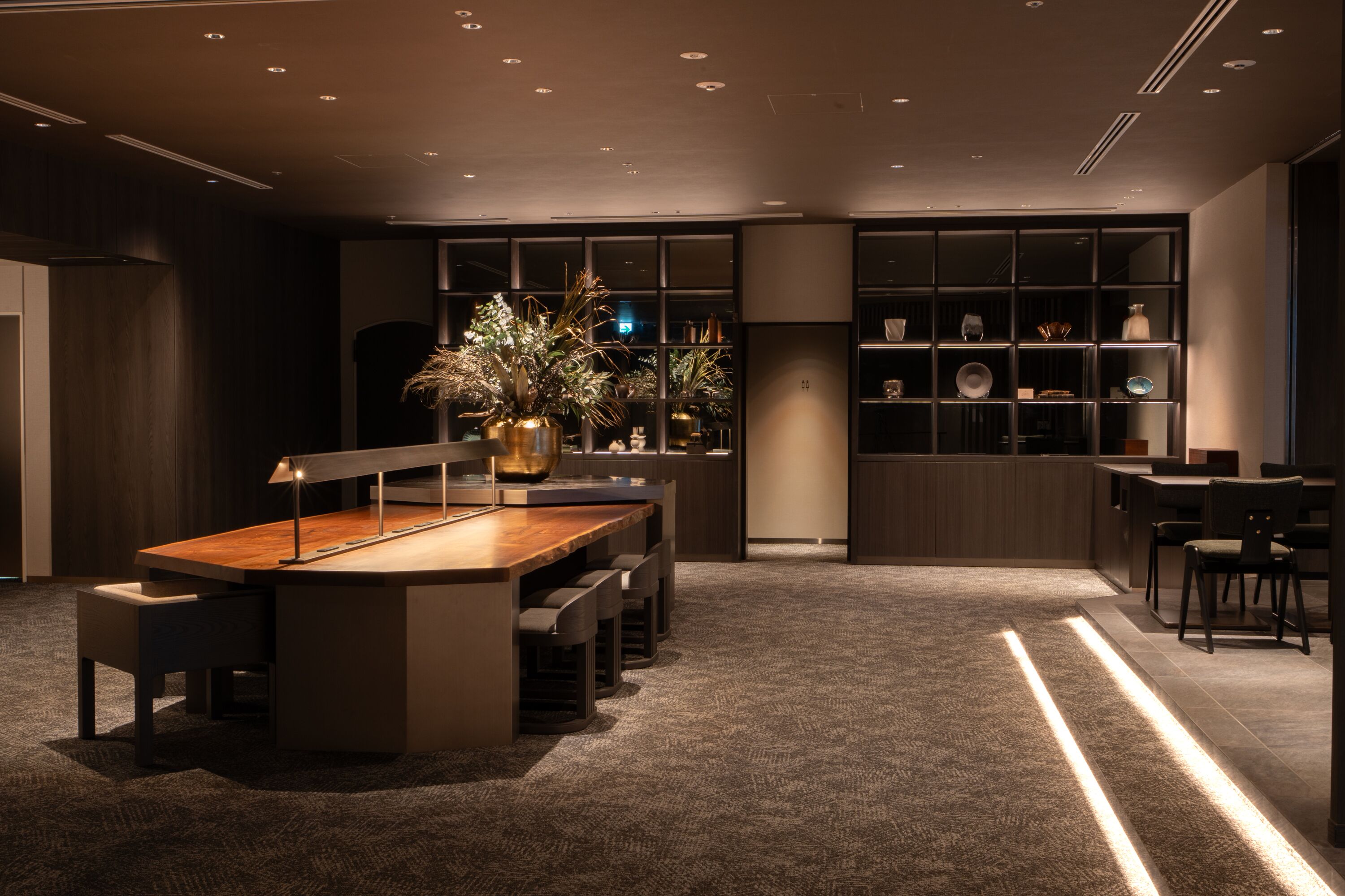 Un interior moderno con una mesa de comedor central, asientos y un centro de mesa decorativo con una planta.