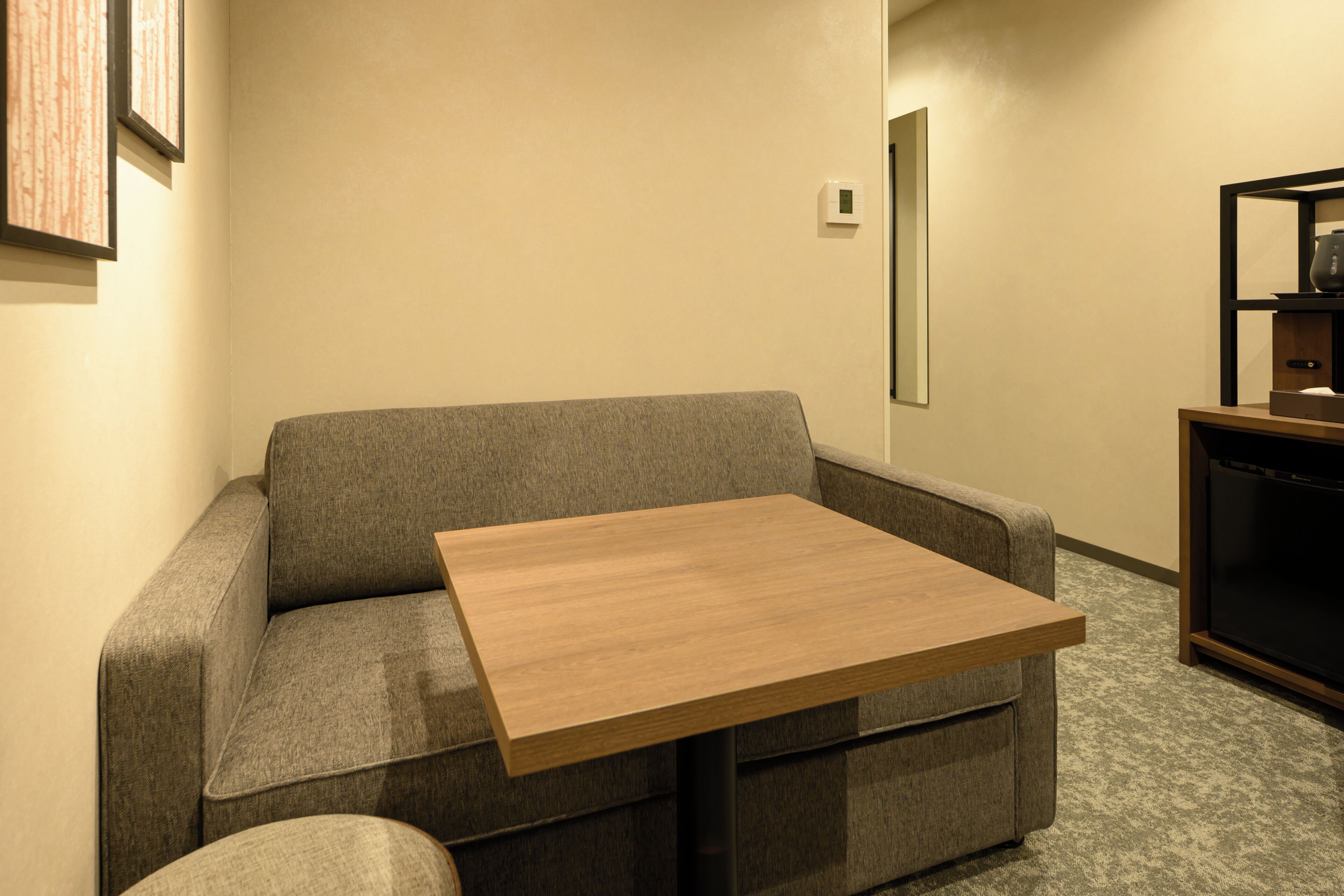 Una habitación con un sofá gris, una mesa de madera, un mueble para televisor y un termostato en la pared.