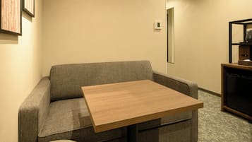 Una habitación con un sofá gris, una mesa de madera, un mueble para televisor y un termostato en la pared.