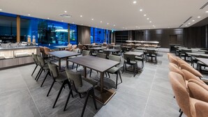 Eine moderne Hotelhalle mit mehreren Sitzbereichen, einer Rezeption und großen Fenstern mit Blick auf das Hotelgebäude.