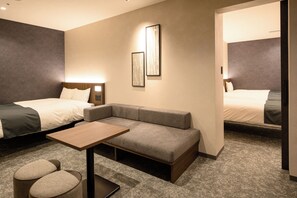 Habitación de hotel con cama, sofá, una mesita y dos otomanes.
