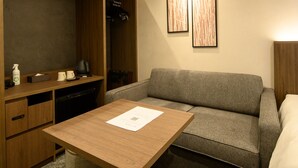 Ein kompaktes Hotelzimmer mit einem Holztisch, einem grauen Sofa und einem Bett.