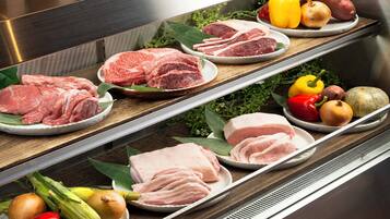 Exhibición de diferentes carnes y verduras en platos, con una encimera de cocina y electrodomésticos de acero inoxidable al fondo.