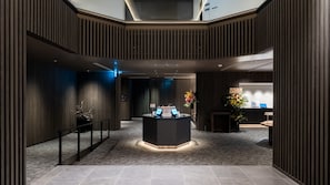 A modern reception area with a reception desk, a digital information kiosk, and a decorative plant. - REGIONIA by Quintessa Sapporo Sta. Front (Sapporo)