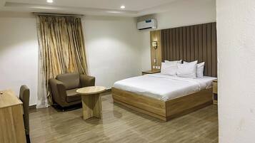 A modern hotel room with a wooden bed, a small round table, a brown leather chair, and a large window with curtains.