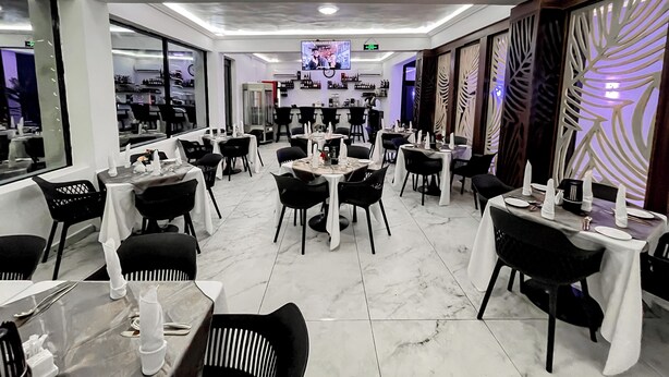 Un restaurant moderne avec un sol en marbre, des tables décorées en noir et blanc et un écran de télévision en arrière-plan.