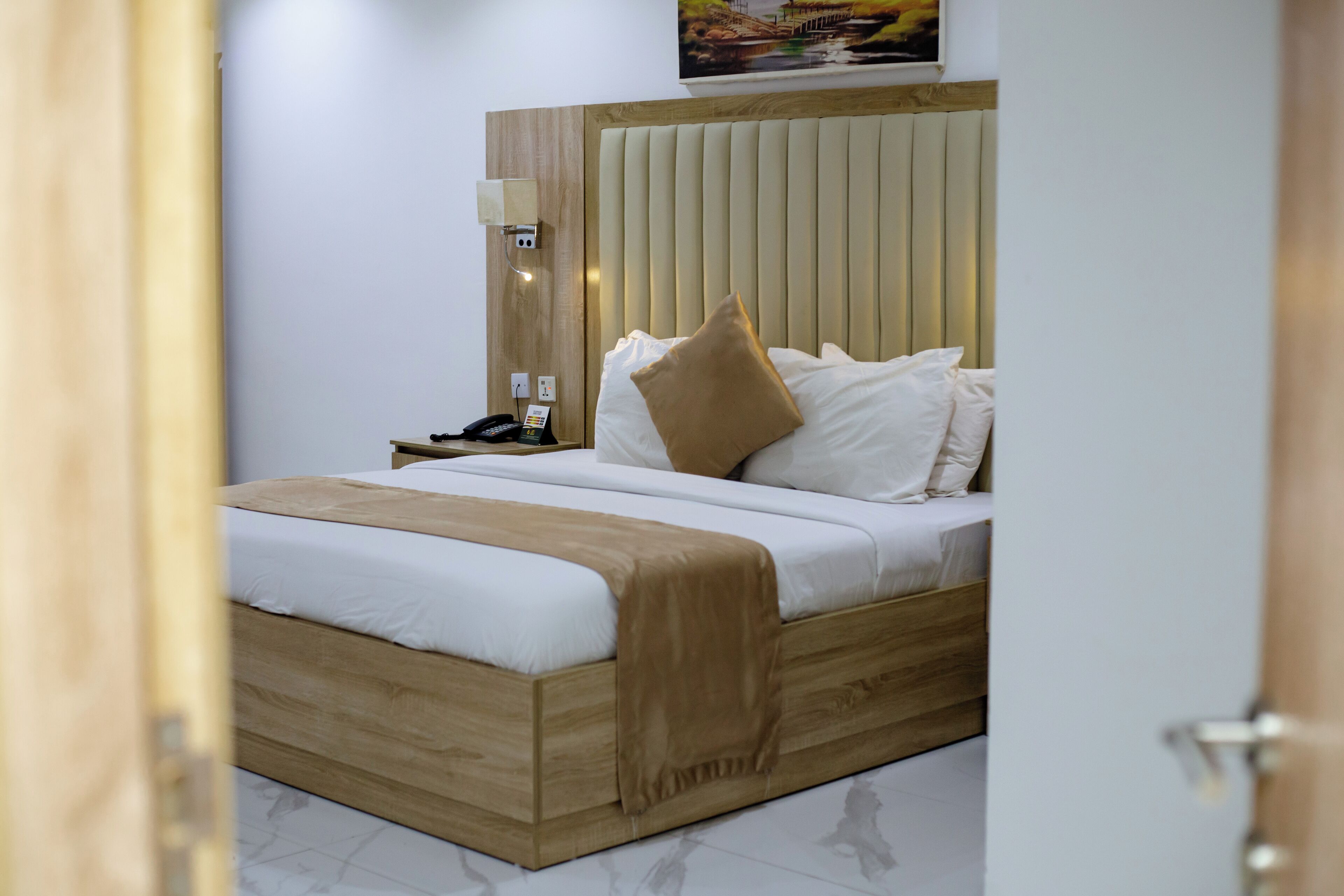 Ein modernes Hotelzimmer mit einem Bettgestell aus Holz, weißer Bettwäsche und einem Kopfteil mit vertikalen Lamellen.