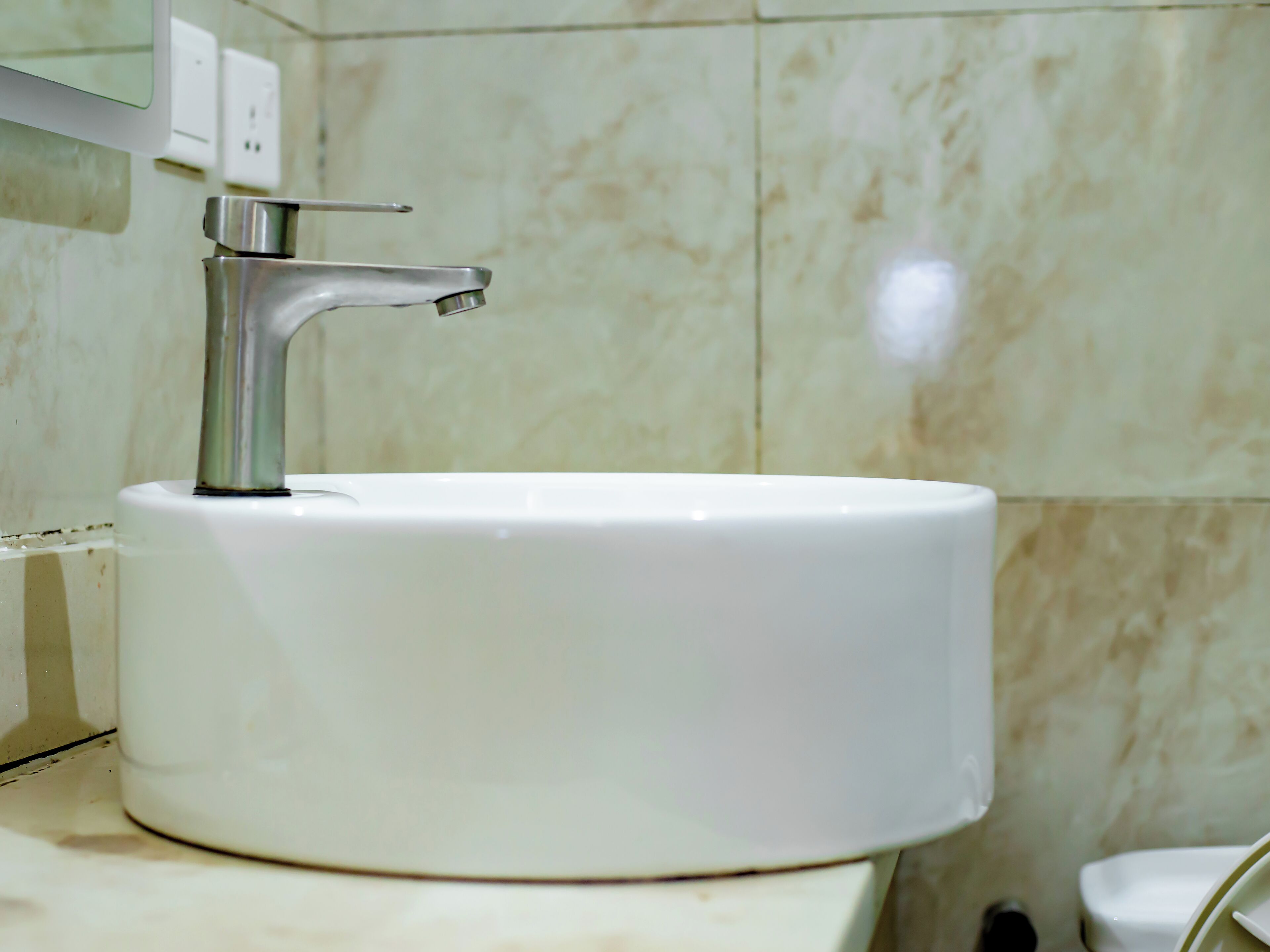 Ein Badezimmer mit einem weißen Waschbecken, einem Chromarmaturen und einer Wand mit Marmorfliesen.
