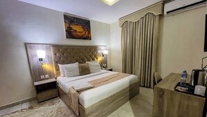 Une chambre d’hôtel avec un grand lit, un bureau, une chaise, une bouteille d’eau et une poubelle.
