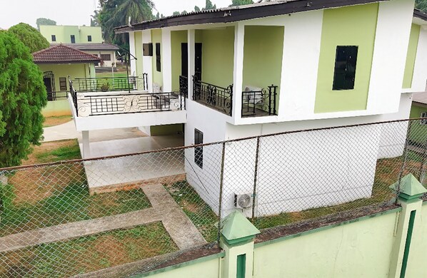 A two-story residential building with a balcony, a fenced yard, and a neighboring house in the background. - OTI RESORT (Benin City)